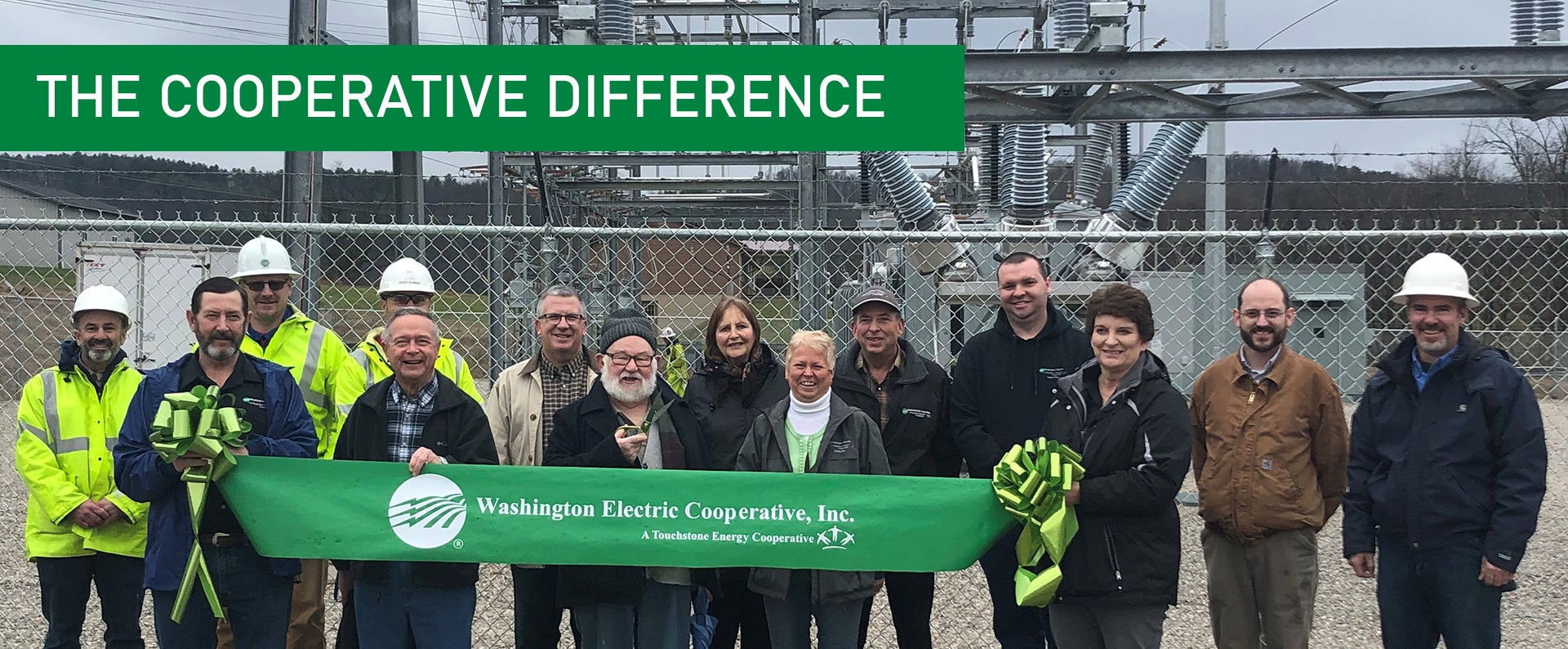 ​  Photo of Washington Electric Cooperative employees, members, and trustees holding a green ribbon in front of the Rouse substation. 